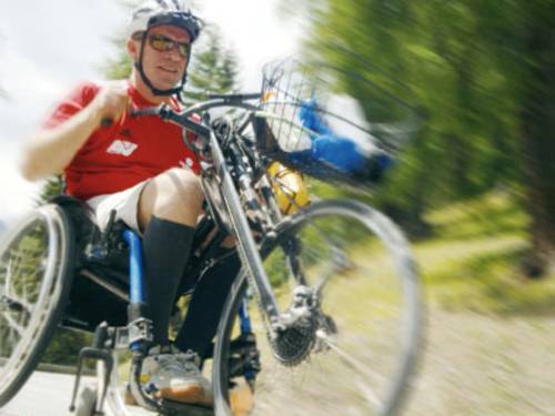 Sportlicher Mann mit Rollstuhlfahrrad rollt mit Geschwindigkeit eine Straße herunter